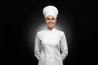 Photo of Happy female chef wearing uniform and cap on black background