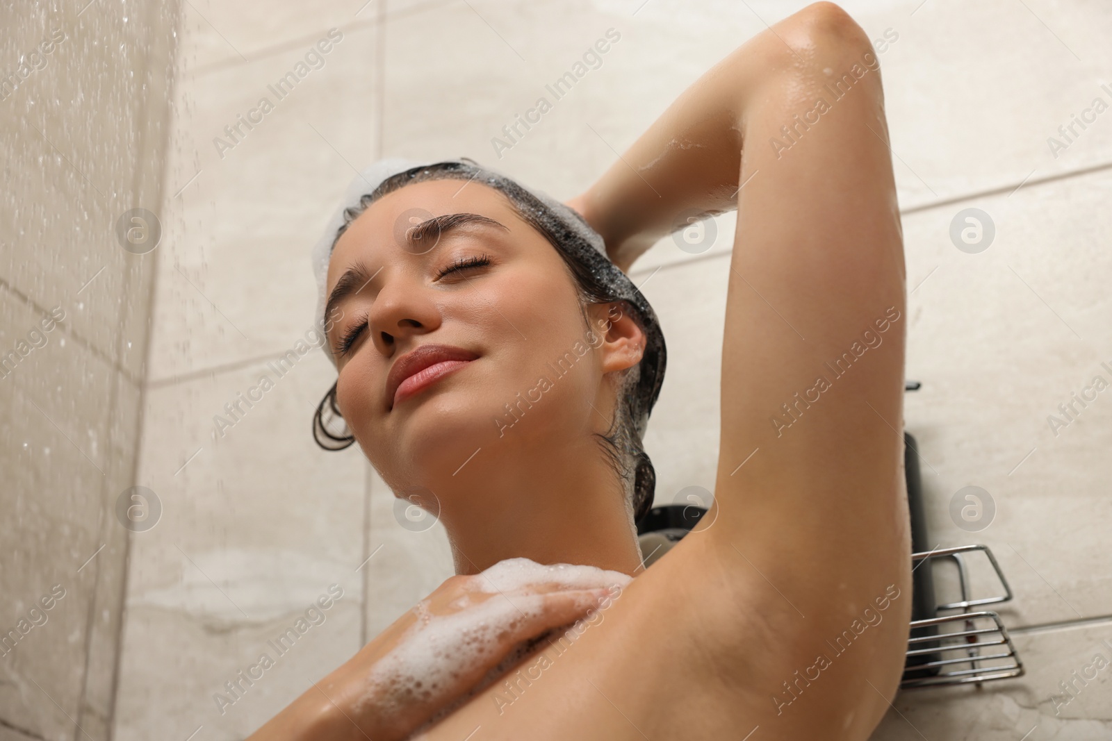 Photo of Beautiful woman washing hair with shampoo in shower, low angle view