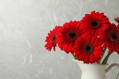 Photo of Bouquet of beautiful red gerbera flowers in ceramic jug on light grey background. Space for text