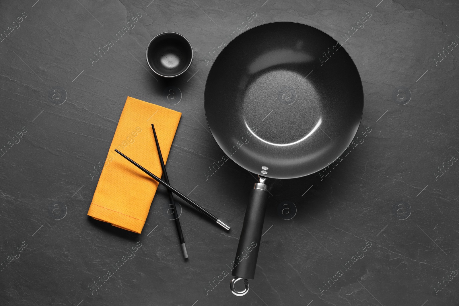 Photo of Empty iron wok, sauce bowl and chopsticks on black table, flat lay