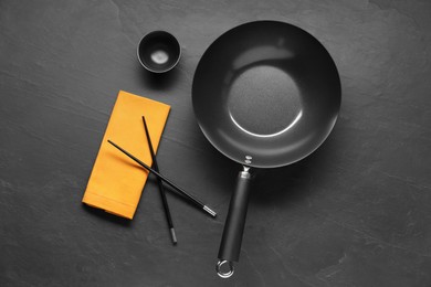 Empty iron wok, sauce bowl and chopsticks on black table, flat lay