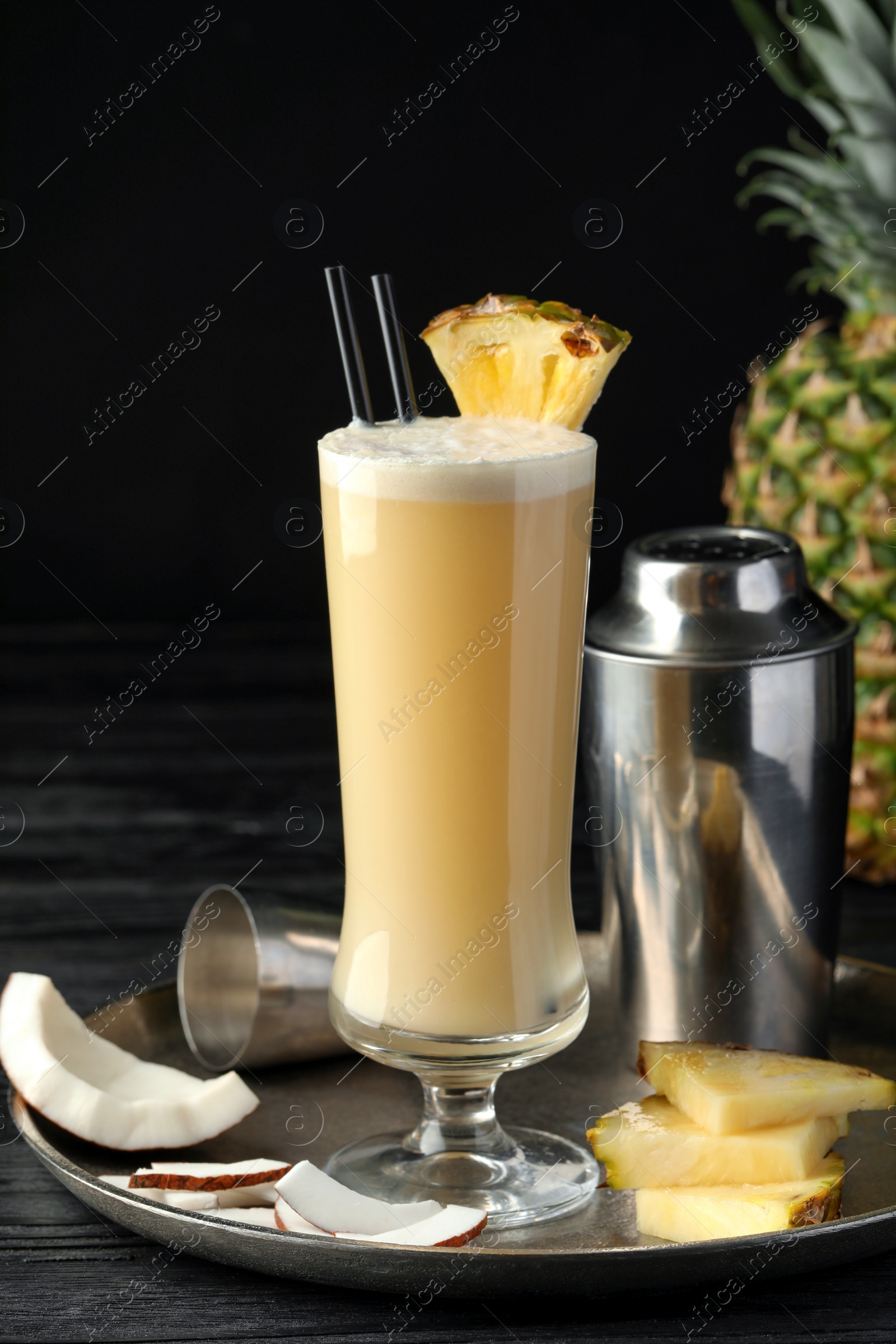 Photo of Tasty Pina Colada cocktail and ingredients on black wooden table