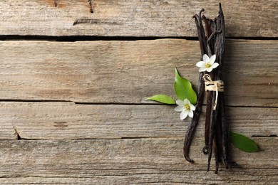 Photo of Bunch of vanilla pods, flowers and leaves on wooden table, top view. Space for text