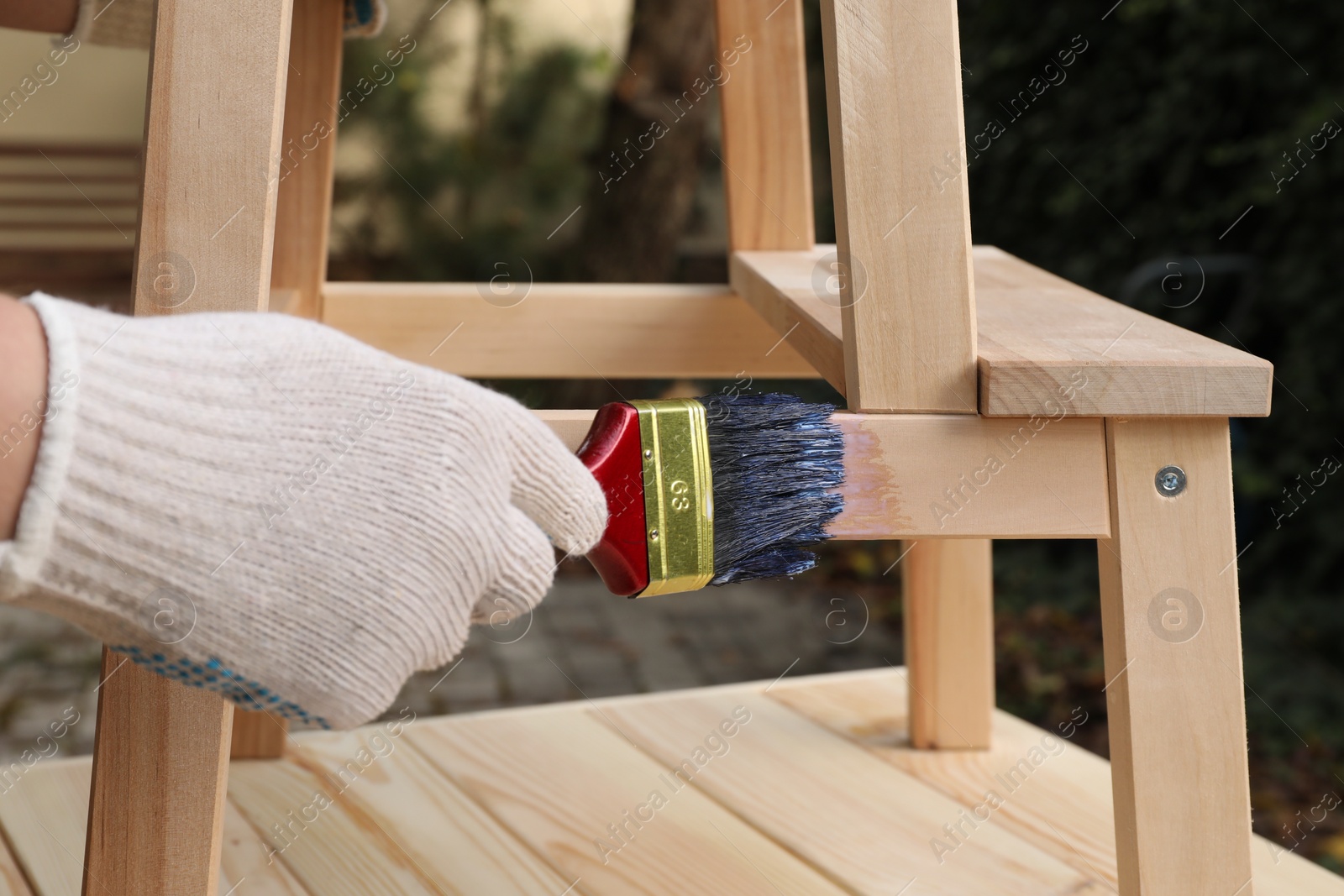 Photo of Man varnishing wooden step stool at table outdoors, closeup