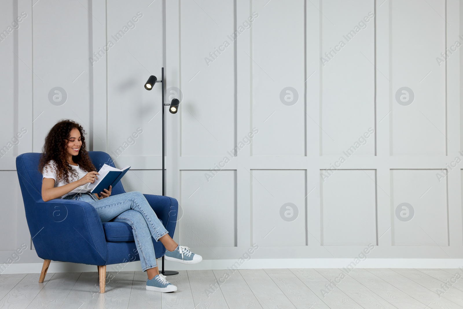 Photo of Young African-American woman reading book in armchair indoors. Space for text