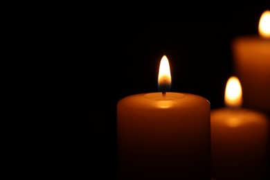 Photo of Burning wax candles on black background, closeup. Space for text