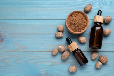 Photo of Bottles of nutmeg oil, nuts and powder on turquoise wooden table, flat lay. Space for text