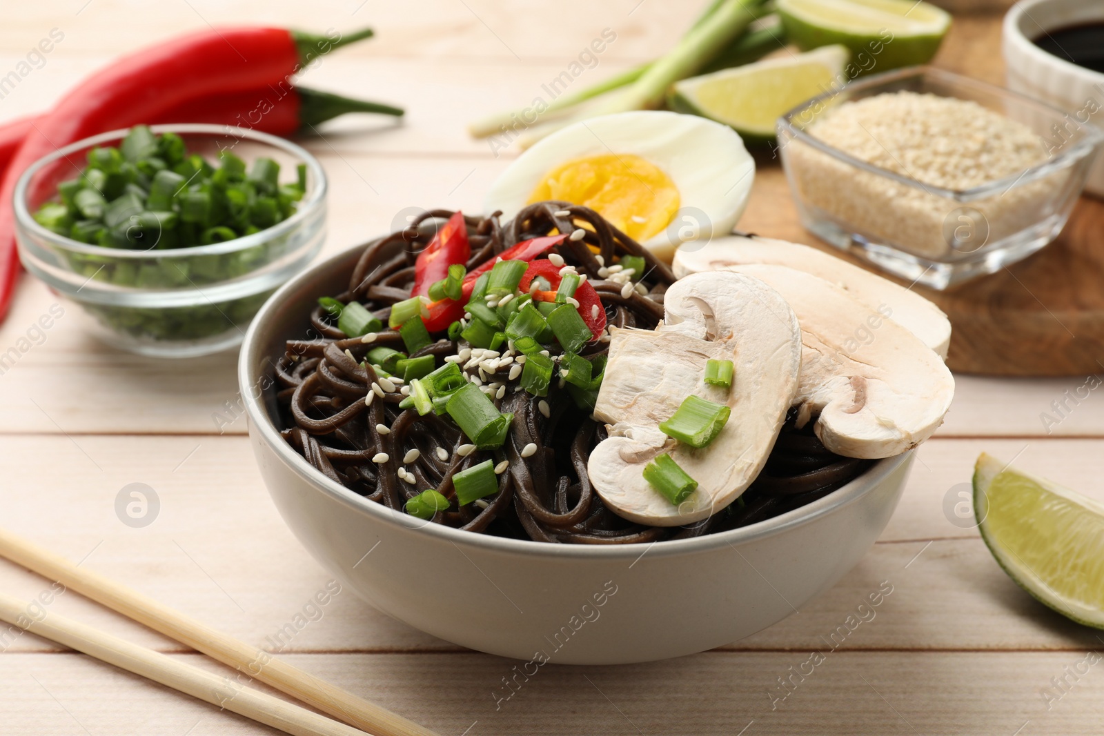 Photo of Tasty buckwheat noodles (soba) with mushrooms, egg and chili pepper served on wooden table, closeup