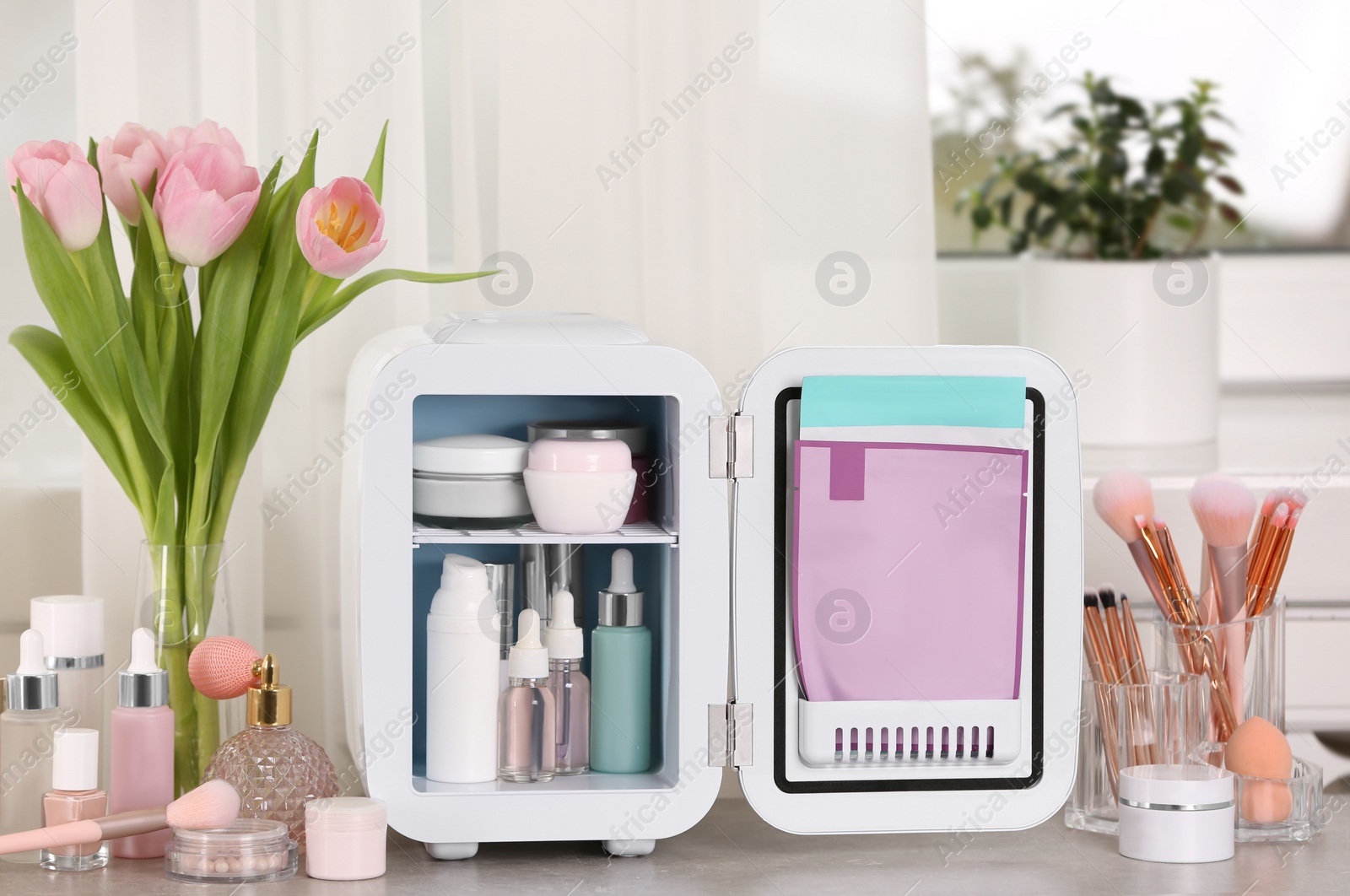 Photo of Open mini cosmetics refrigerator and skin care products on table