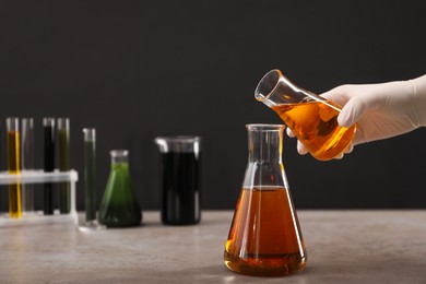 Photo of Woman pouring yellow crude oil into flask at grey table against dark background, closeup