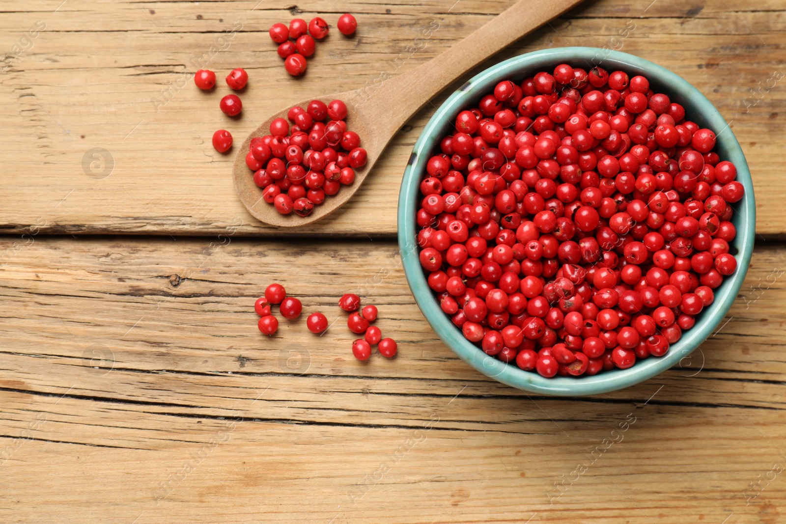 Photo of Aromatic spice. Red pepper in bowl and spoon on wooden table, top view. Space for text