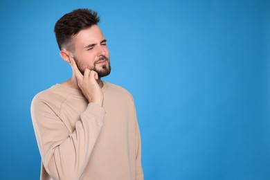 Photo of Young man suffering from ear pain on light blue background. Space for text