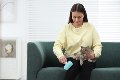 Photo of Pet shedding. Woman with lint roller removing cat`s hair from trousers on sofa at home, space for text