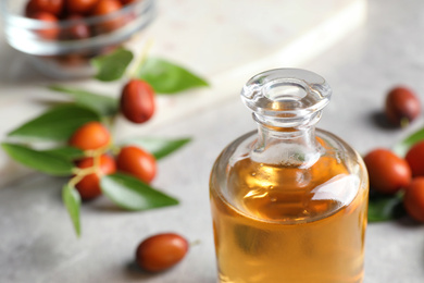 Jojoba oil in glass bottle on table, closeup view