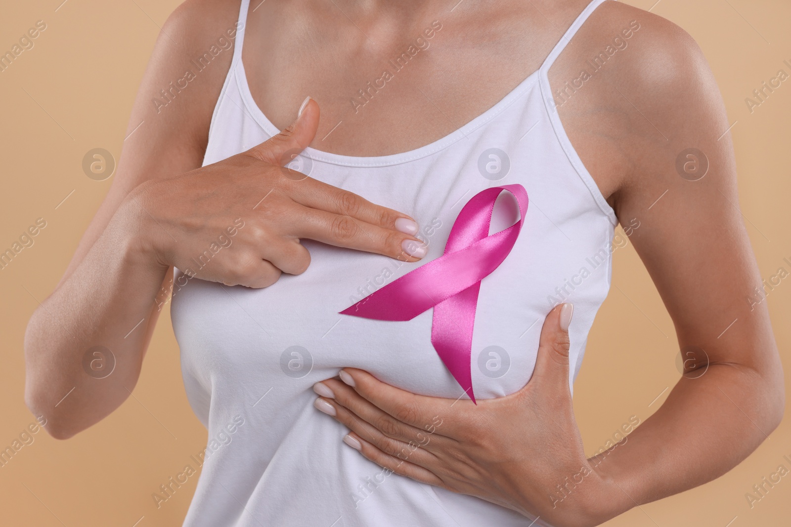 Photo of Breast cancer awareness. Woman with pink ribbon doing self-examination on light brown background, closeup