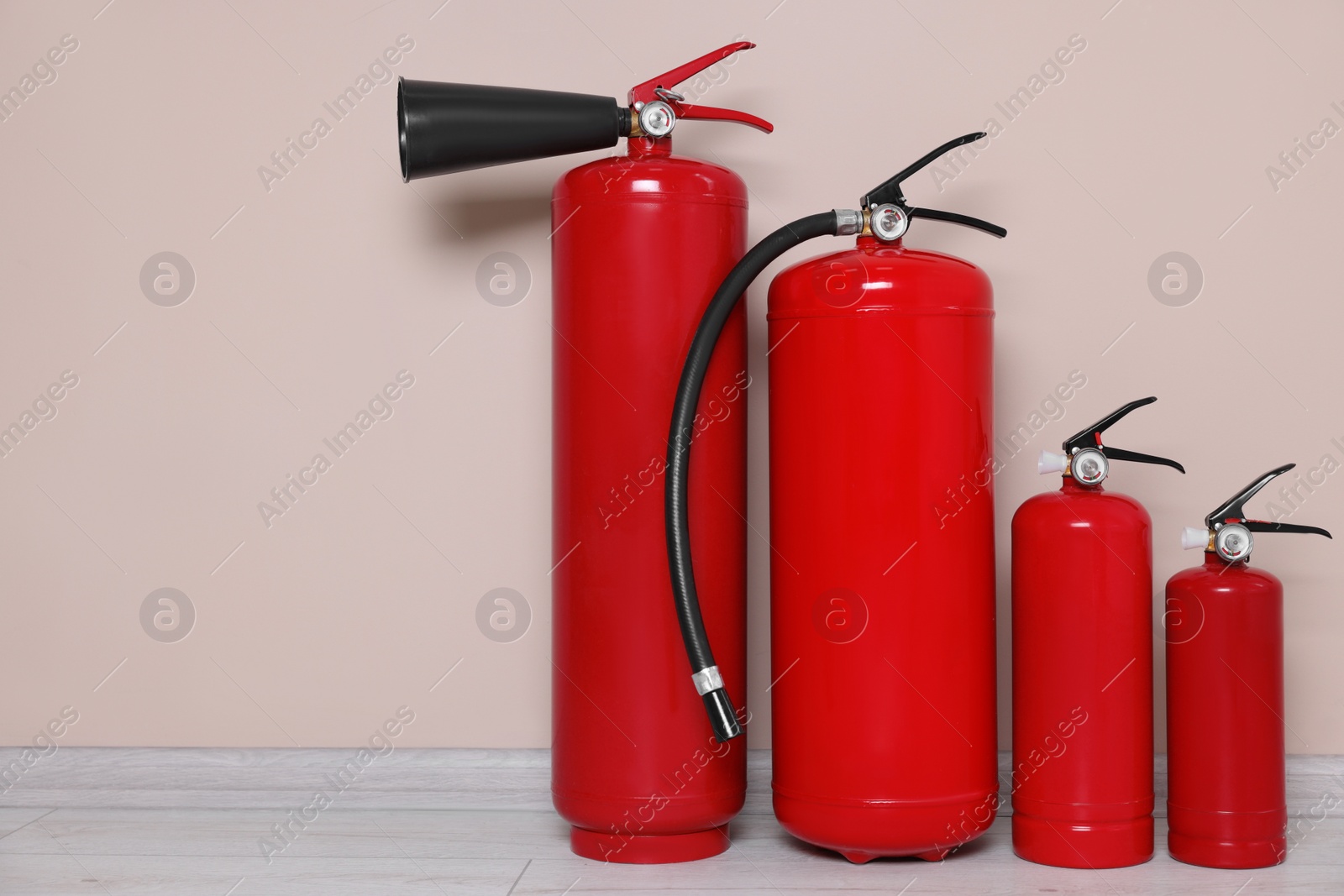 Photo of Set of fire extinguishers on floor near beige wall, space for text