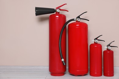 Photo of Set of fire extinguishers on floor near beige wall, space for text