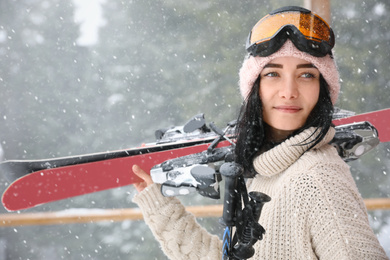 Photo of Young woman with skis wearing winter sport clothes and goggles outdoors