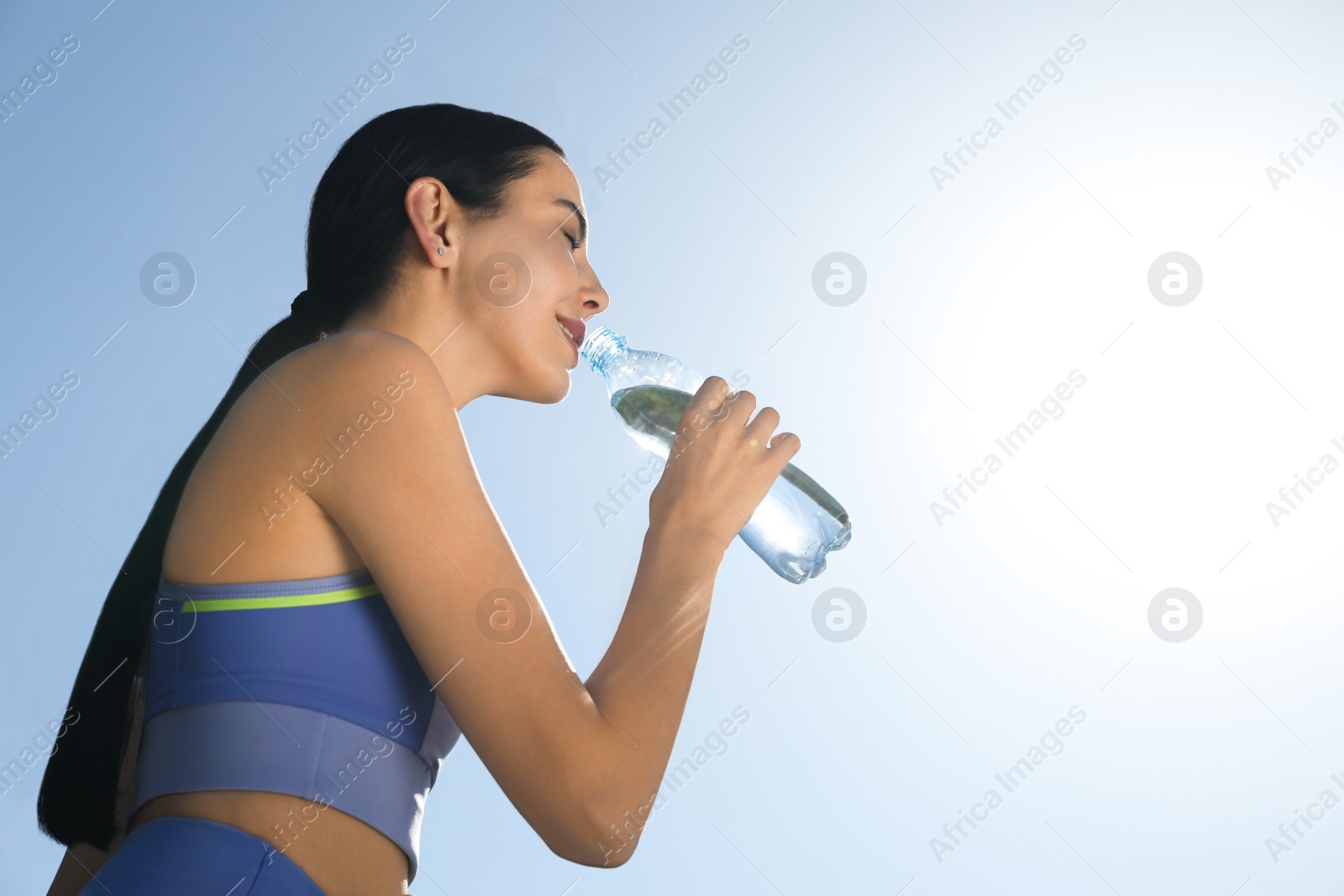 Photo of Beautiful young sportswoman drinking water outdoors. Refreshing drink