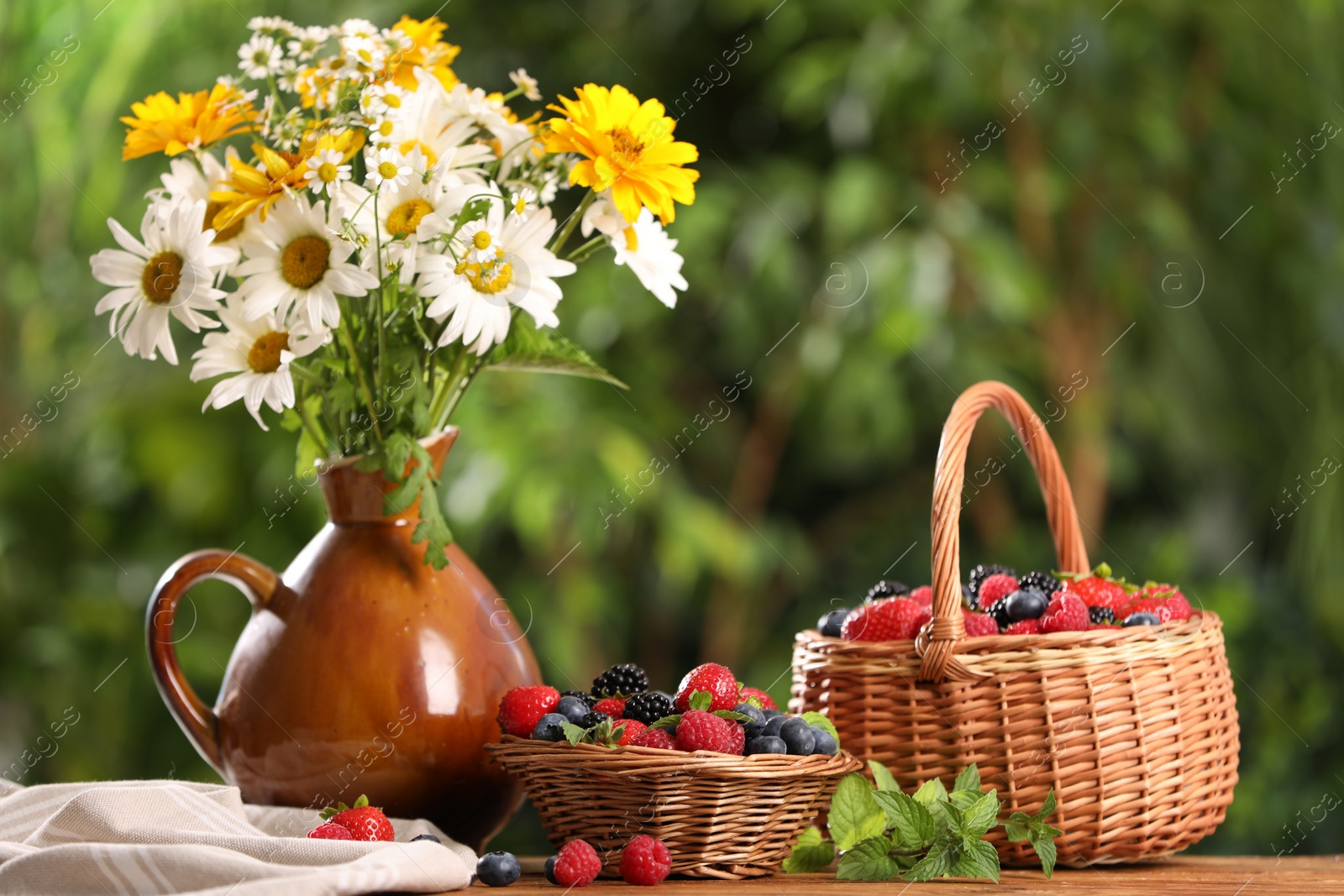 Photo of Different fresh ripe berries and beautiful flowers on table outdoors