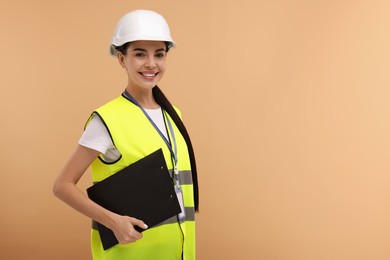 Photo of Engineer in hard hat holding clipboard on beige background, space for text