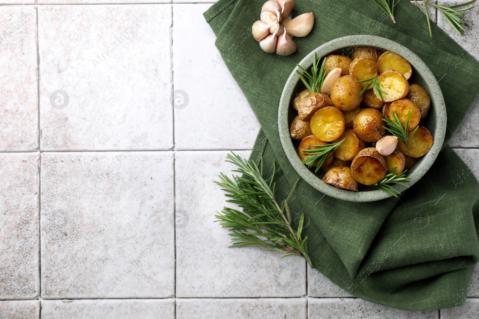 Photo of Bowl with tasty baked potato and aromatic rosemary on light tiled table, flat lay. Space for text