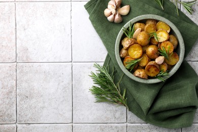 Bowl with tasty baked potato and aromatic rosemary on light tiled table, flat lay. Space for text