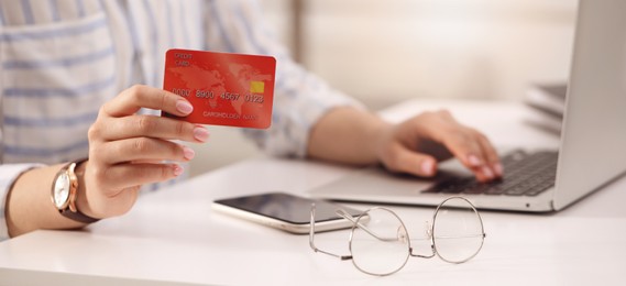 Woman with credit card using laptop for online payment at table, closeup. Banner design