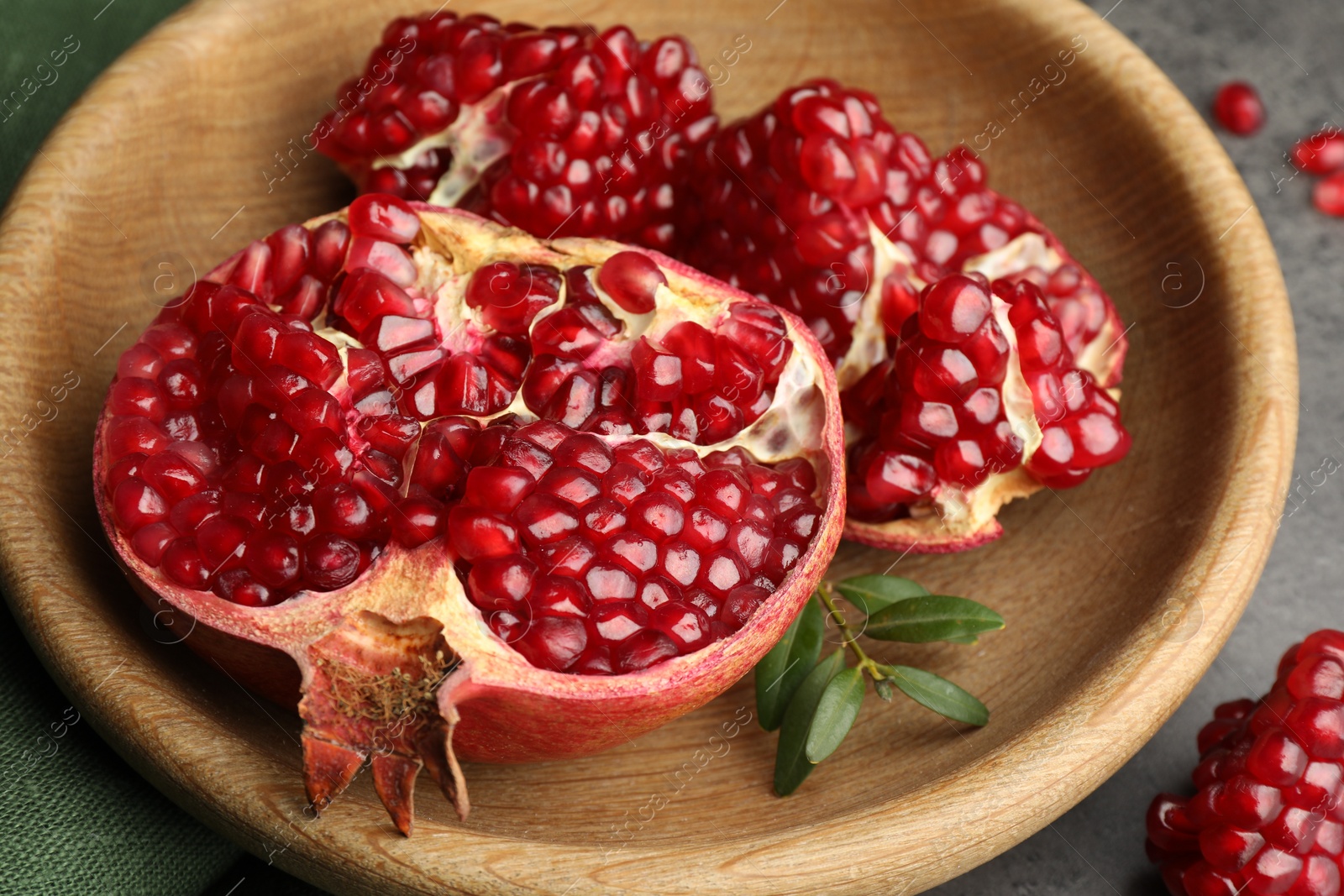 Photo of Cut fresh pomegranate and green leaves on grey table, closeup