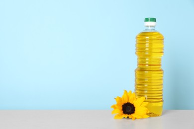 Photo of Bottle of cooking oil and sunflower on white table, space for text