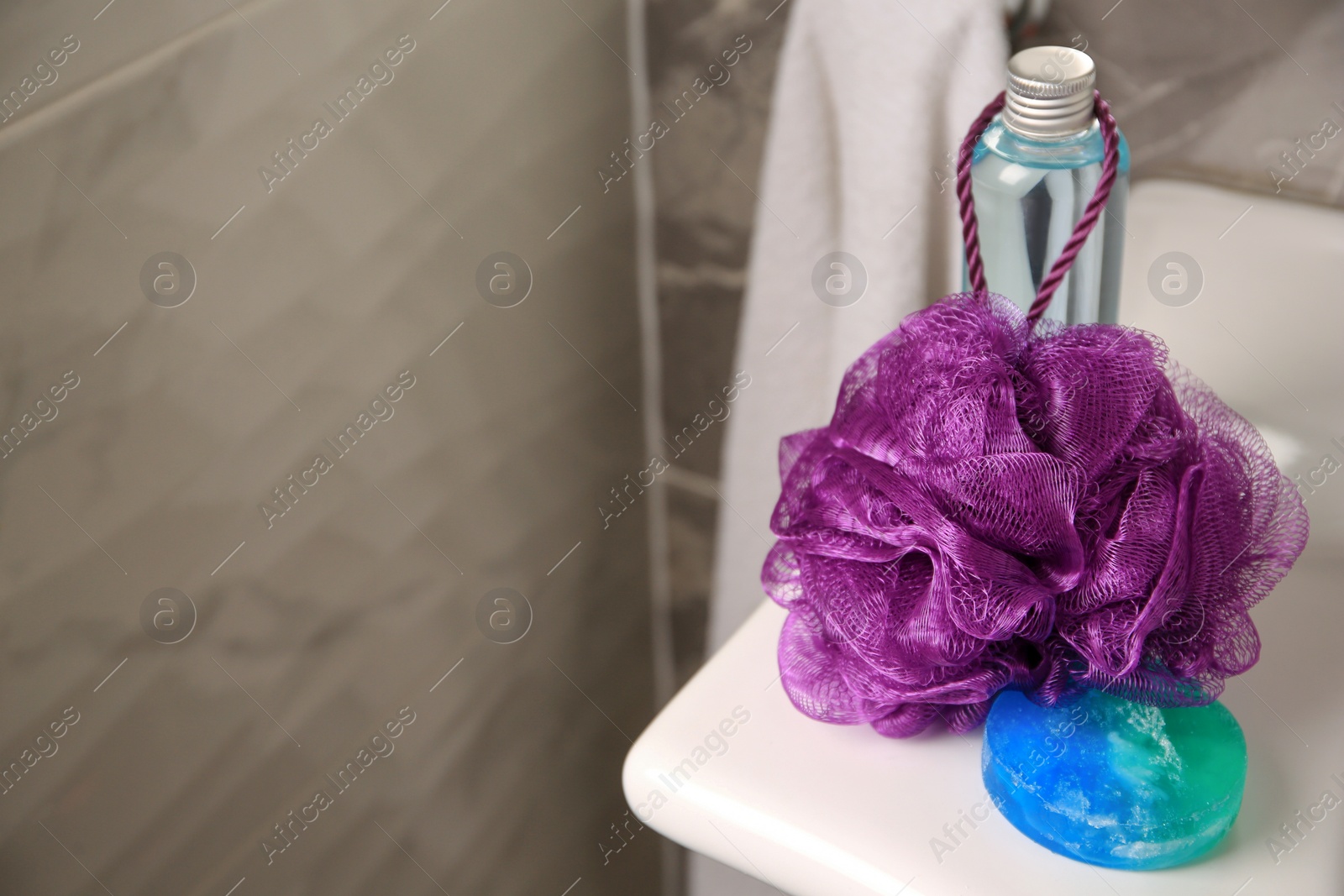 Photo of Purple shower puff and cosmetic products on sink in bathroom, space for text