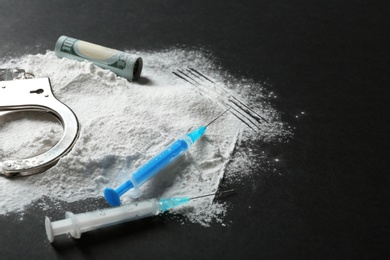 Composition with heap of cocaine and syringes on black background