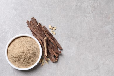 Dried sticks of liquorice root and powder on grey table, flat lay. Space for text