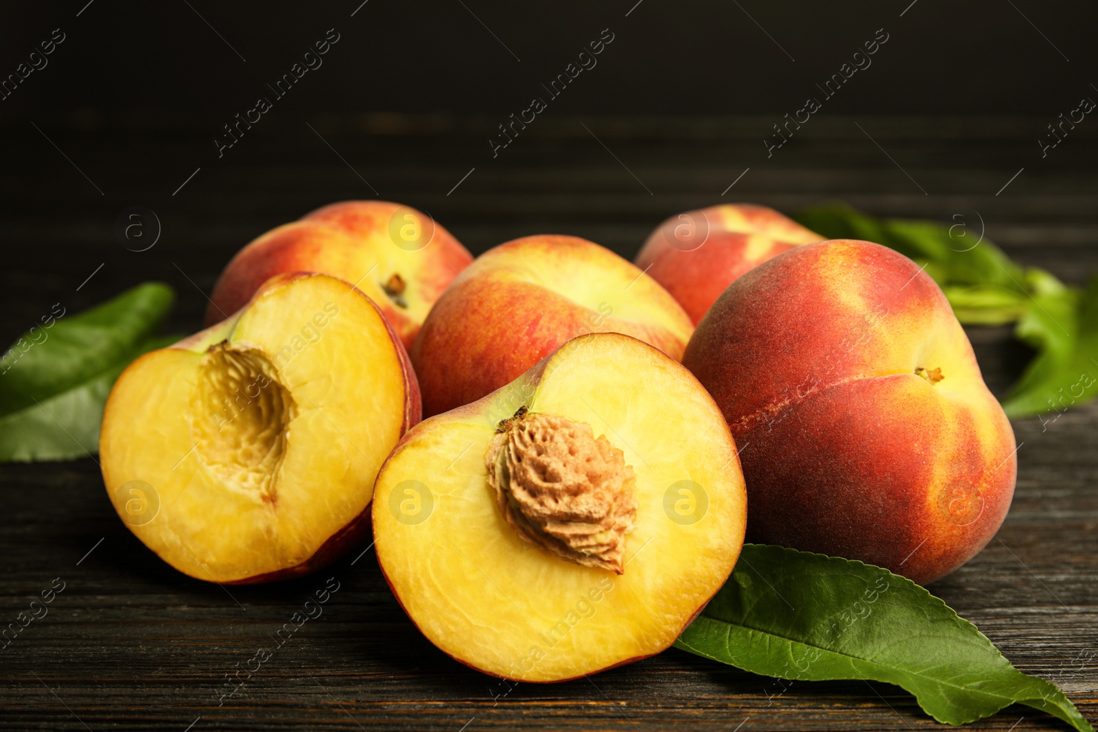 Photo of Fresh juicy peaches and leaves on black wooden table