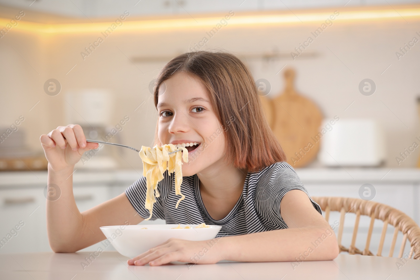 Photo of Happy girl eating tasty pasta at table in kitchen