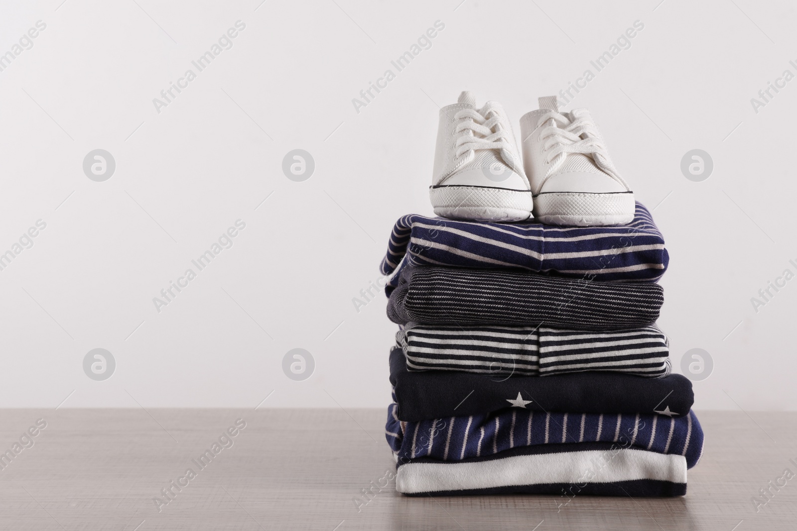 Photo of Stack of baby boy's clothes and shoes on wooden table against white background, space for text