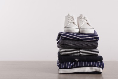 Photo of Stack of baby boy's clothes and shoes on wooden table against white background, space for text