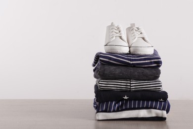 Stack of baby boy's clothes and shoes on wooden table against white background, space for text