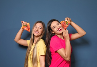 Attractive young women with slices of delicious pizza on color background