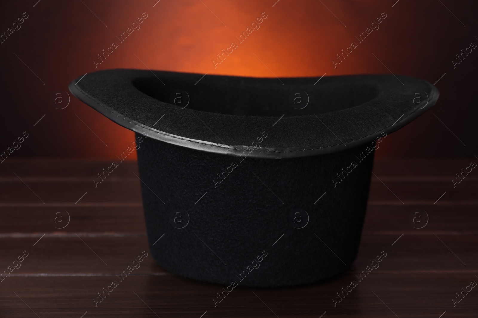 Photo of Black magician top hat on wooden table against color background, closeup