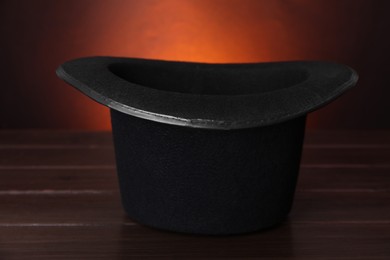 Black magician top hat on wooden table against color background, closeup