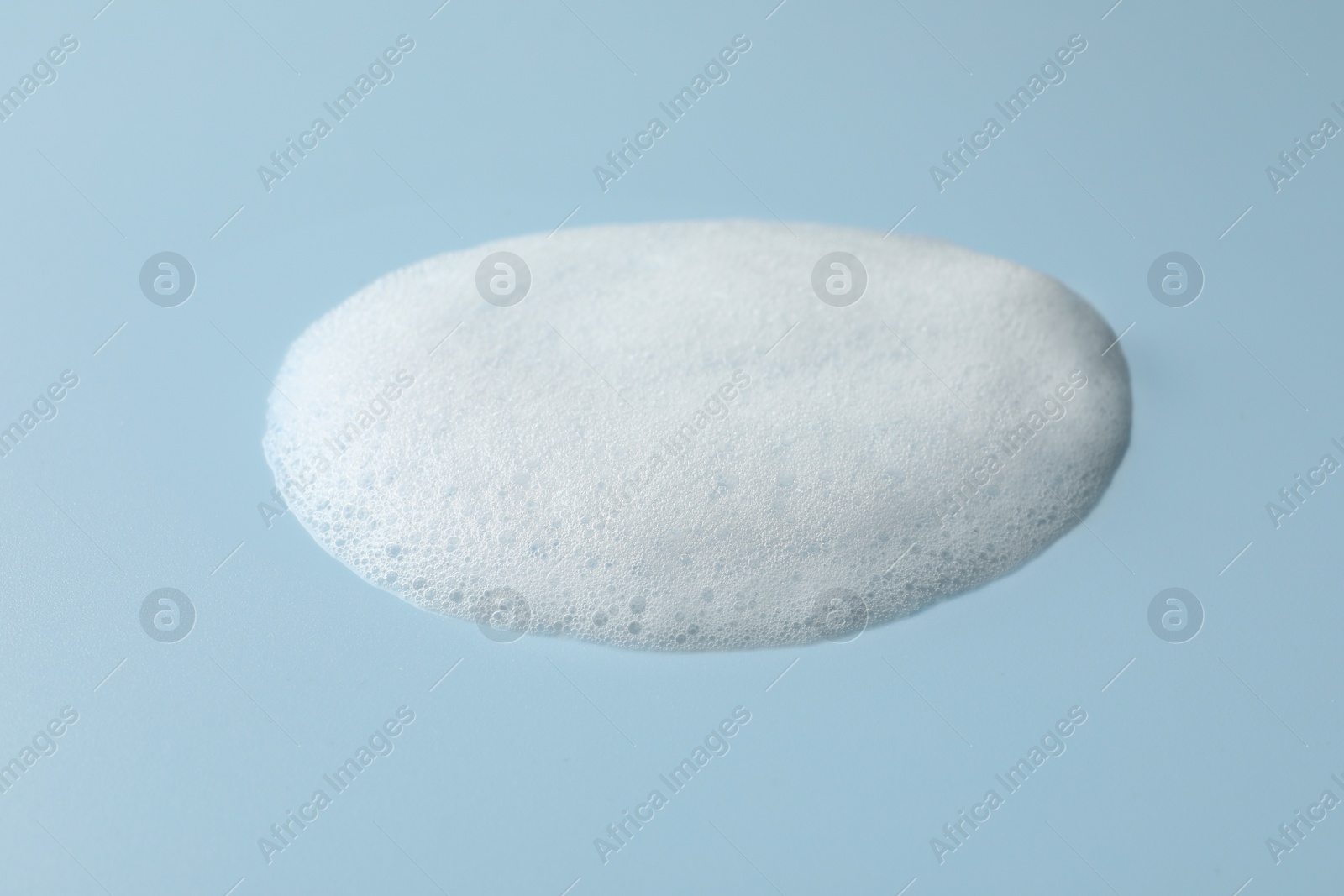 Photo of Drop of fluffy soap foam on light blue background