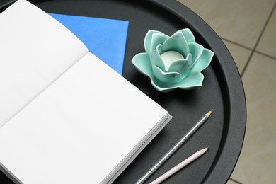 Photo of Notebooks, pencils and decorative holder with candle on round table indoors, closeup
