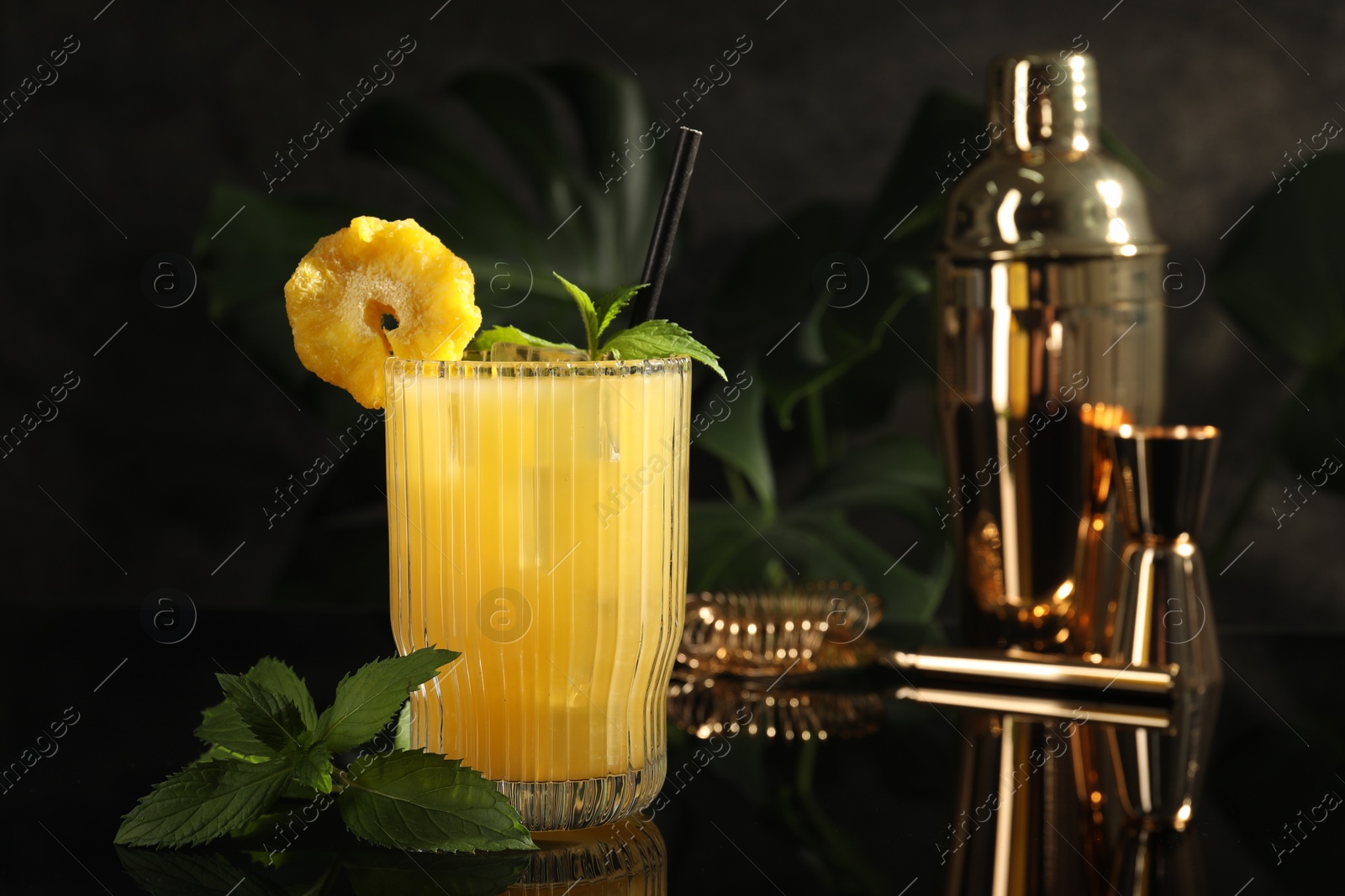 Photo of Tasty pineapple cocktail with mint on black mirror surface