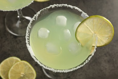 Photo of Delicious Margarita cocktail with ice cubes in glass and lime on grey table, above view