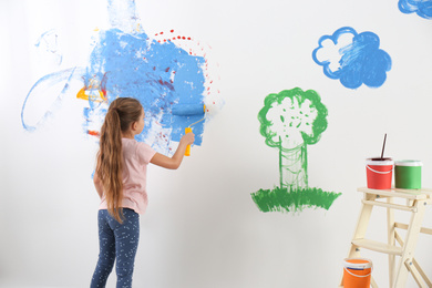 Photo of Little child painting wall with roller brush indoors