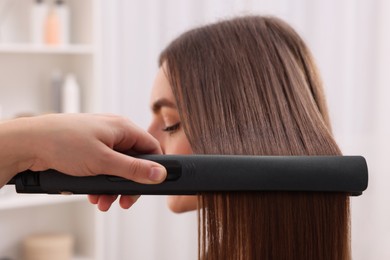 Photo of Hairdresser straightening woman's hair with flat iron in salon, selective focus