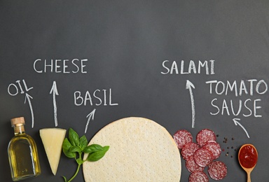 Pizza crust, ingredients and chalk written product's names on black background, flat lay