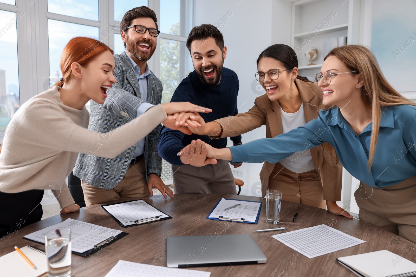 Photo of Team of employees joining hands in office