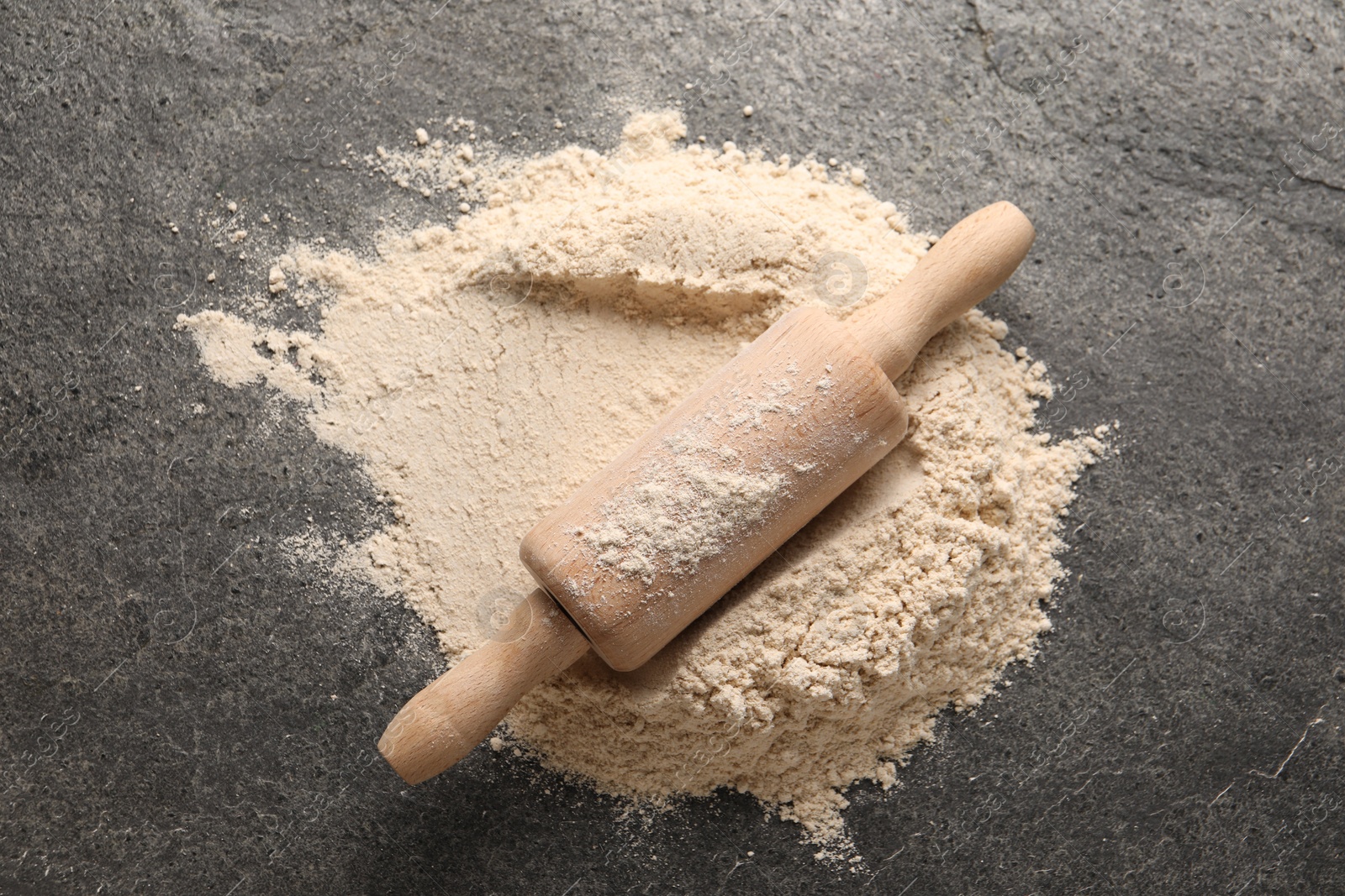 Photo of Scattered flour and rolling pin on grey textured table, top view